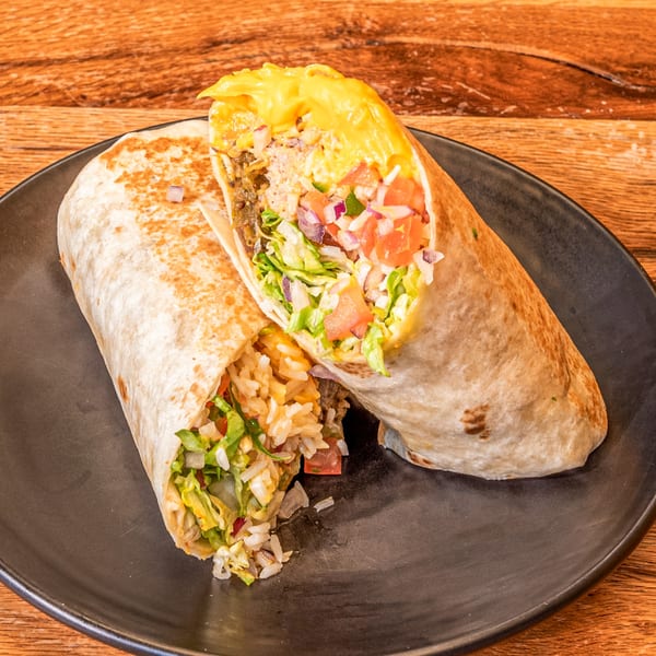Two Los Comparres burritos, one cut open to show rice, meat, lettuce, tomato, and cheese sauce.