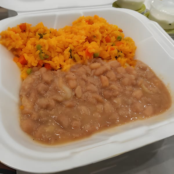 Mexican rice with peas and carrots next to a serving of refried beans in a white to-go container.