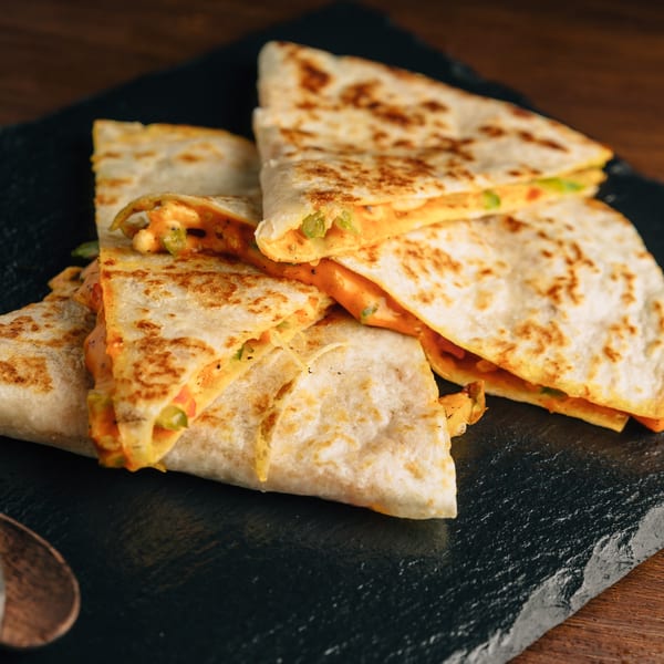 Several cheesy quesadilla triangles with green peppers on a dark slate board at Los Comparres.